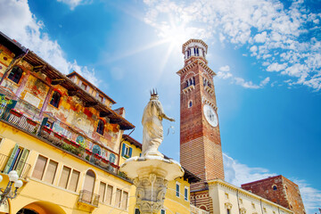 Fountain statue of Madonna and Lamberti tower with clock on Erbe Square. Torre dei Lamberti. Famous clock tower in Piazza delle Erbe. Travel Destination Verona Italy - obrazy, fototapety, plakaty
