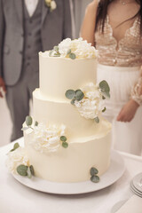 The wedding cake. Wedding Cake with blur bride and groom background. Wedding cake with luxury decorated in wedding party. White, three-tiered, decorated with flowers.