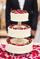 The wedding cake. Wedding Cake with blur bride and groom background. Wedding cake with luxury decorated in wedding party. White, three-tiered, decorated with flowers.
