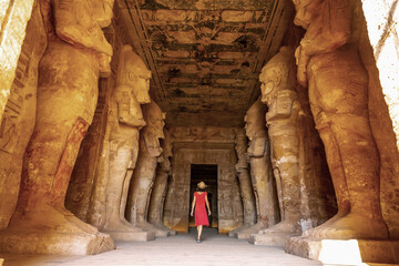 A young woman in a red dress at the Abu Simbel Temple next to the sculptures, in southern Egypt in Nubia next to Lake Nasser. Temple of Pharaoh Ramses II, travel lifestyle - obrazy, fototapety, plakaty