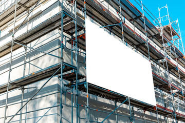 Blank white advertisement hanging on the scaffolding of modern building under construction.Reconstruction of a building with white billboard. - obrazy, fototapety, plakaty