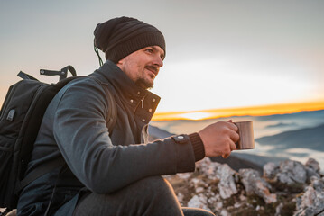 A happy man traveler drinking a cup of coffee during the hiking on the mountain.