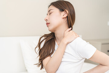 Pain body muscles stiff problem, asian young woman painful with back, neck ache from work hand holding massaging rubbing shoulder hurt, sore sitting on bed in room at home. Health care and medicine.