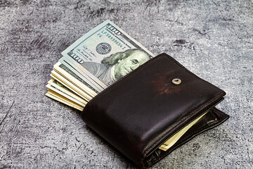 100 american dollar banknotes sticking out of a leather wallet.
