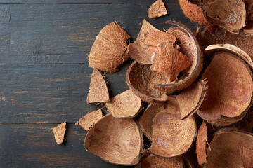 pieces of coconut fruit shell on black wooden surface, commercially important strong and durable fibrous material, used as fuel source, ingredient in various products, taken from above with copy space