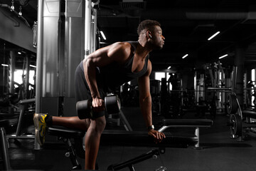 Obraz na płótnie Canvas athletic african american man trains in dark gym, athletic guy lifts heavy dumbbells in fitness club