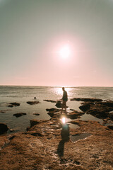 Podróżnik o zachodzie słońca na tle oceanu stojący przy skałach. - obrazy, fototapety, plakaty