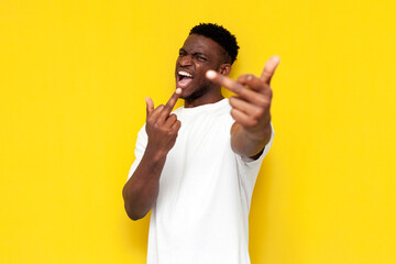 rude african american man showing middle finger at camera and yelling on yellow isolated background