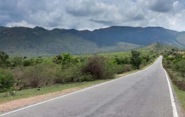  A Dramatic view of a deserted country road leading towards a Picturesque landscape of Mountain range  against the romantic cloudscape in Karnataka, India.