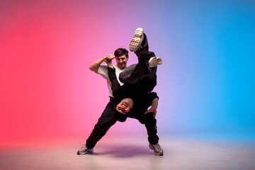 two dancer guys break dance on red blue background and do trick together, male acrobats perform pair dance in neon