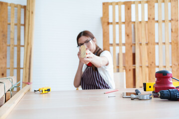 Female carpenter using tape measure and tools to craft wood project in workshop, highlighting...
