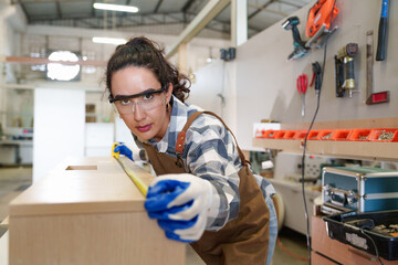 Young Caucasian carpenter woman measuring plank wood on the desk factory for the production of...