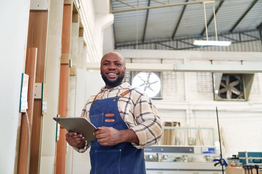 Portrait of African American carpenter man workers standing using digital tablet to mark on plywood board and work in carpentry workshop factory. Production CNC line of the wooden working factory