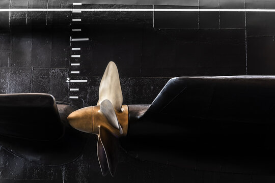 Huge shiny submarine propeller and draft scale on black hull, close up
