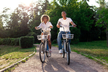 Obraz premium african-american couple rides bicycles in the park and talks, man and woman walk on eco-transport
