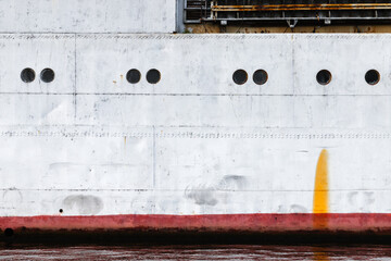 Old ship hull with red waterline and portholes, industrial transportation background