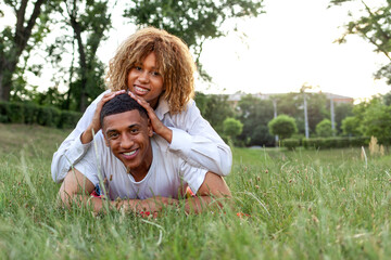 Obraz premium african american young couple in love lies together on the grass in the park in the summer and smiles