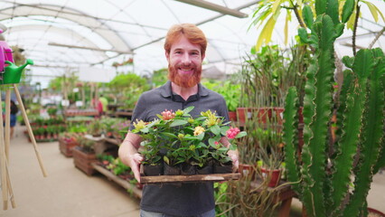 Portrait of a male caucasian redhead customer holding basket of plants and flowers inside horticultural greenhouse plant store
