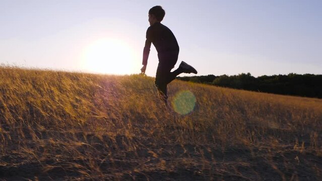 The silhouette of a happy boy at sunset. A child runs through a meadow, a park. rising up towards the sun. The concept of a child dream. Side view