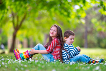 Happy kids boy and girl in rain rubber boots playing outside in the green park with blooming field...