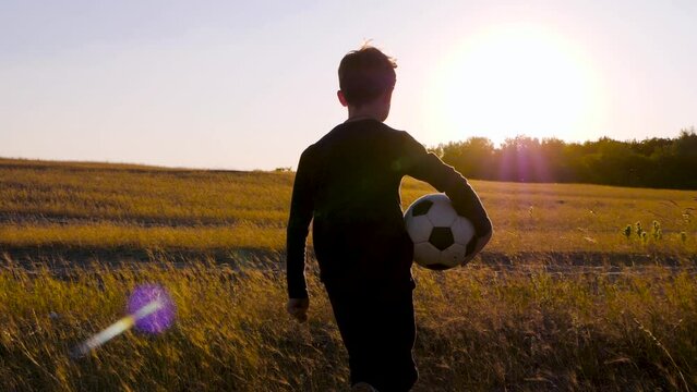 Silhouette of a happy boy at sunset. A child runs through a meadow and holds a ball in his hands. The concept of a child dream. children in sports SSTKHome