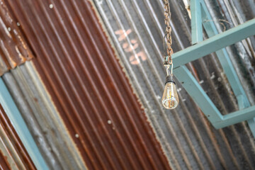 A retro ceiling lightbulb which is hanging from rusty zinc sheet roof of the old factory warehouse...