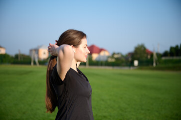 Portrait of young attractive fit girl in black sports tight clothes standing on green field before...
