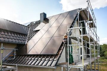 Technician working on a solar panel at a construction site of a single family house - obrazy, fototapety, plakaty