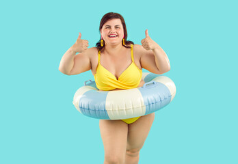 Portrait of happy smiling fat woman in beach rubber ring wearing yellow swimsuit showing thumb up...