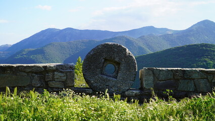 Round stone millstones on the background of green hills in Greece - obrazy, fototapety, plakaty
