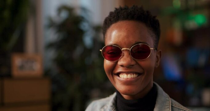 In captivating image African woman sporting stylish pink sunglasses with captivating smile, engaging directly with the camera confident demeanor hints at self-assured nature and sociable character.
