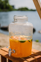 Orange juice in jar or jug. Picnic with wooden decor . Bachelorette party on beach. Boho style design picnic. Decorations for celebration birthday. Wedding outdoors. Summer spring picnic with blanket