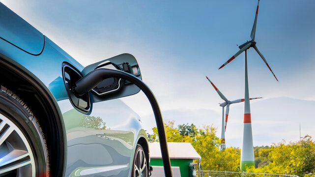 Electric car refueling with wind farm towers in the background. Sustainable and renewable energy.
