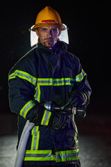 Firefighter using a water hose to eliminate a fire hazard. Team of female and male firemen in dangerous rescue mission. 