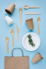Stack of eco-friendly disposable tableware. Wooden forks and knives, paper cups and plates against green background. Biodegradable cutlery and dishes for picnics, takeaways. Copy space. Top view