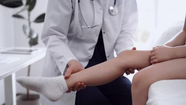 Doctor and patient are in the clinic. Orthopedic in white coat examines knee joint of a kid girl, close up. Medicine, physical therapy concept