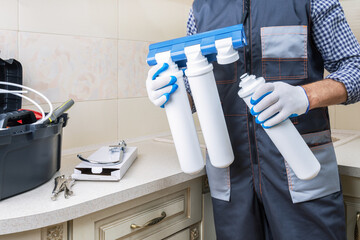 Plumber man installs or change water filter in the kitchen.