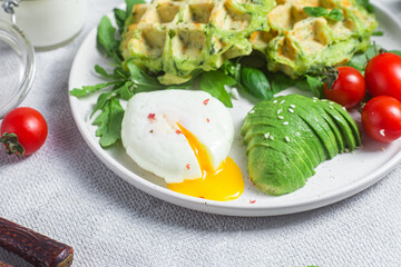 Zucchini waffles, poached egg, avocado and cherry tomatoes in a plate