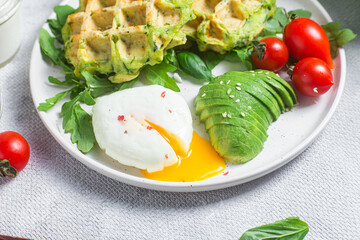 Zucchini waffles, poached egg, avocado and cherry tomatoes in a plate