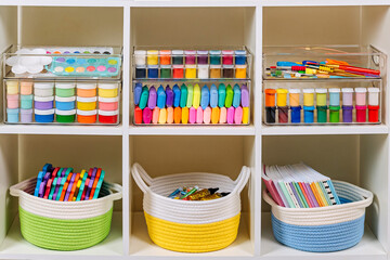 White shelving with kids backpack and various material for creativity and art activity. Stationery...