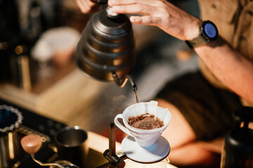 Barista making drip coffee with hot water being poured from a kettle, Ground coffee beans contained...