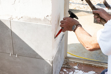 the mason prepares the wall with a chisel before laying a ceramic tile