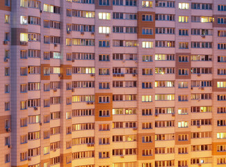 The facade of an apartment building with luminous and dark windows in the late evening.
