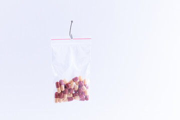 The Pharmaceutical Trap and Drug Addiction - Colored Pills or Tablets Hanging in Small Ziplock Bag on a Fishing Hook Against the White Background