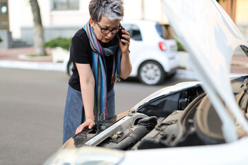 Mature woman talking on the phone and calling technical assistance for a car.