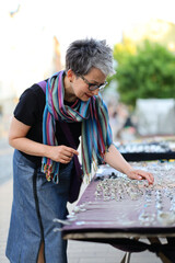 Senior gray-haired woman chooses jewelry at a flea market, vertically.