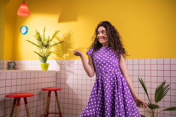 Young looking woman in a beautiful pink dress dancing and moving charismatic in front of the camera in a retro kitchen de star the end she jumping and split legs
