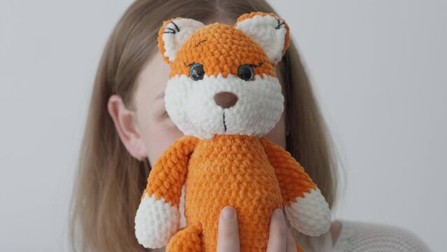 The hobby of knitting homemade toys. With refined taste and skill, a needlewoman creates soft textile toys, admiring her skills. The fox and the face of a young woman.