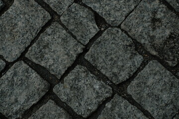 View from above onto stone pavement of urban street. Grass sprouts between tiles