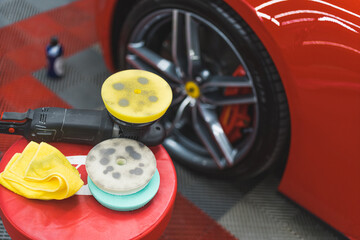 Specialistic deep-cleaning and car detailing products such as microfibre cloth and polishing sponge in front of red sports car. Indoor shot. Focus on the foreground. High quality photo